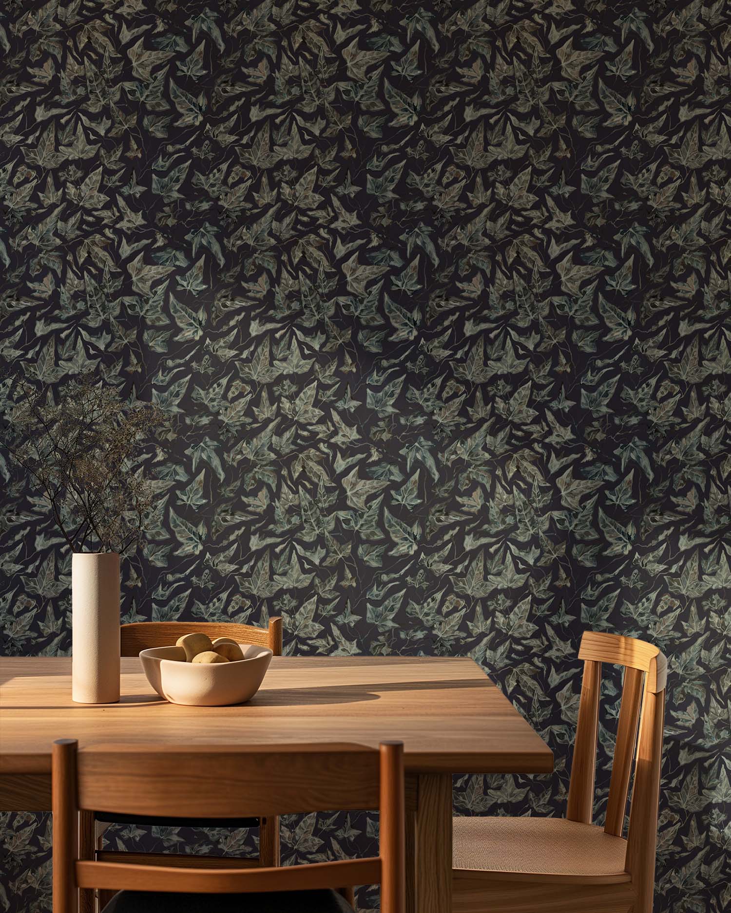 Dining area with wooden table and chairs against a wall covered in a dark ivy pattern wallpaper.