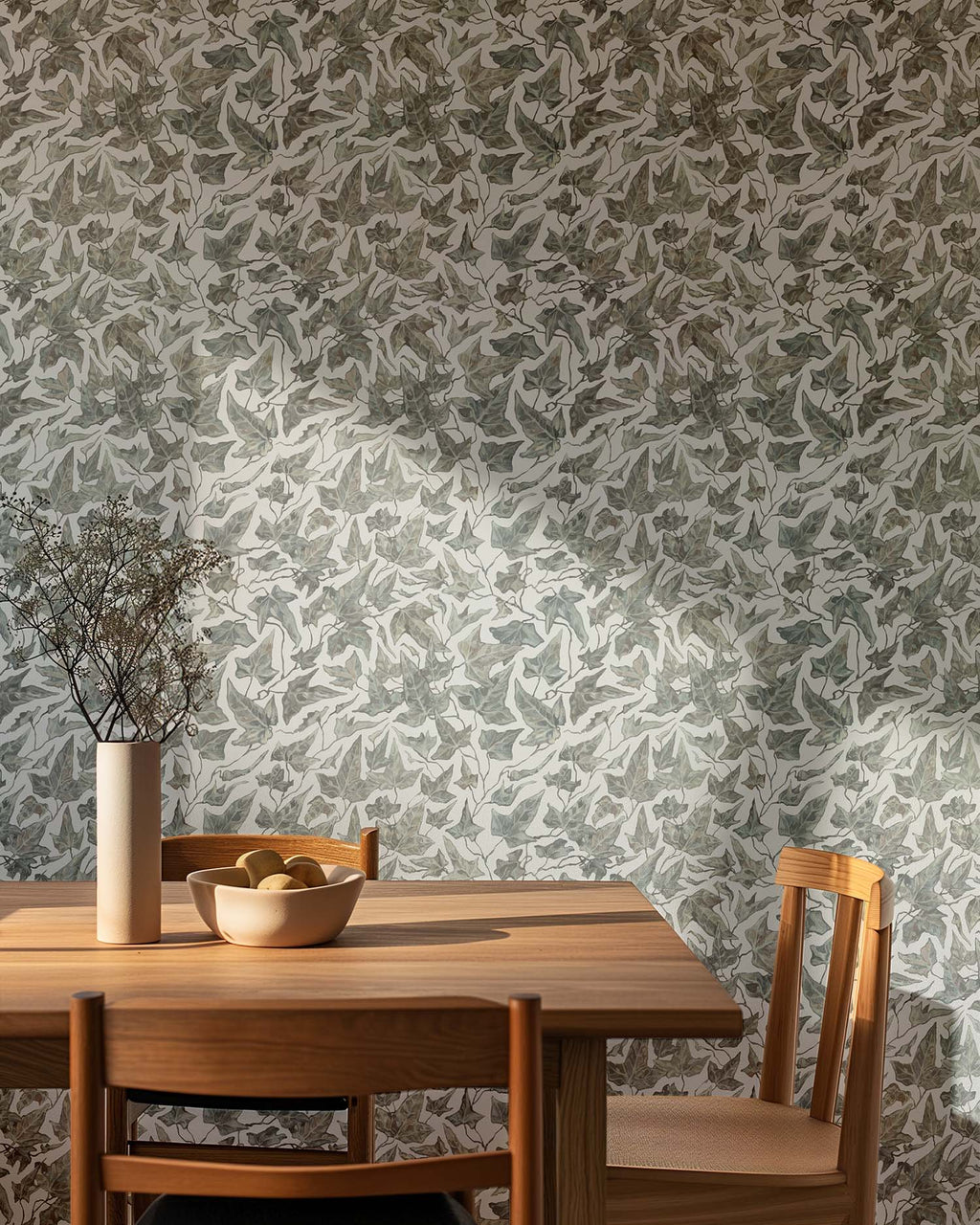 Dining area with wooden table and chairs against a wall covered in a white ivy pattern wallpaper.
