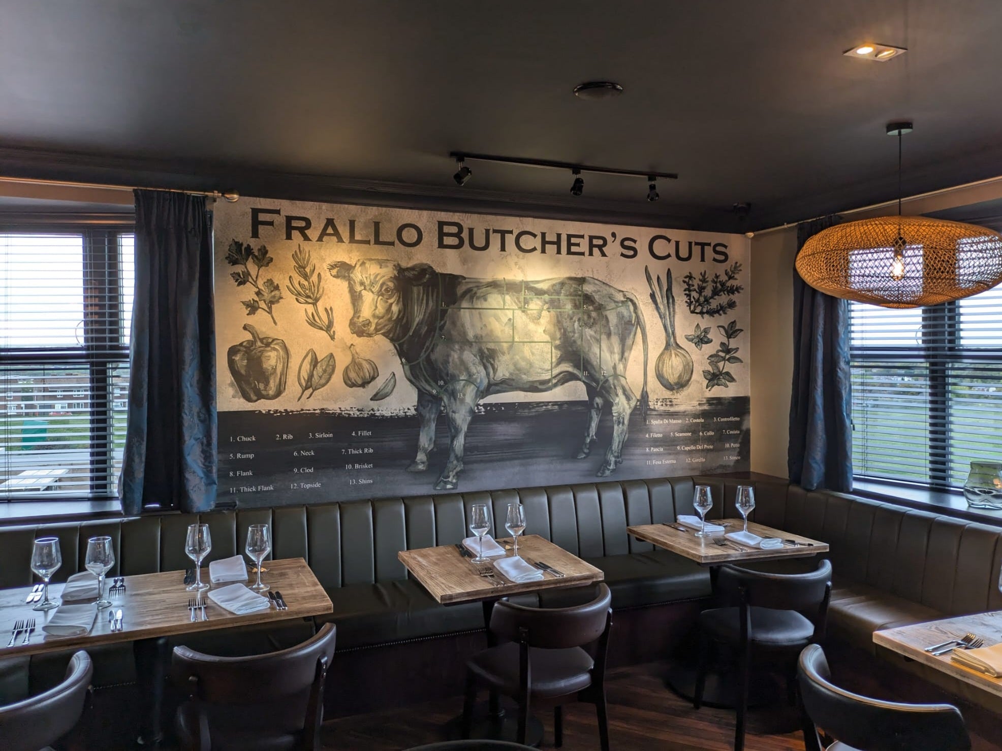 Restaurant interior with painted wall mural of a cow and text saying 'Frallo Butcher's Cuts'.