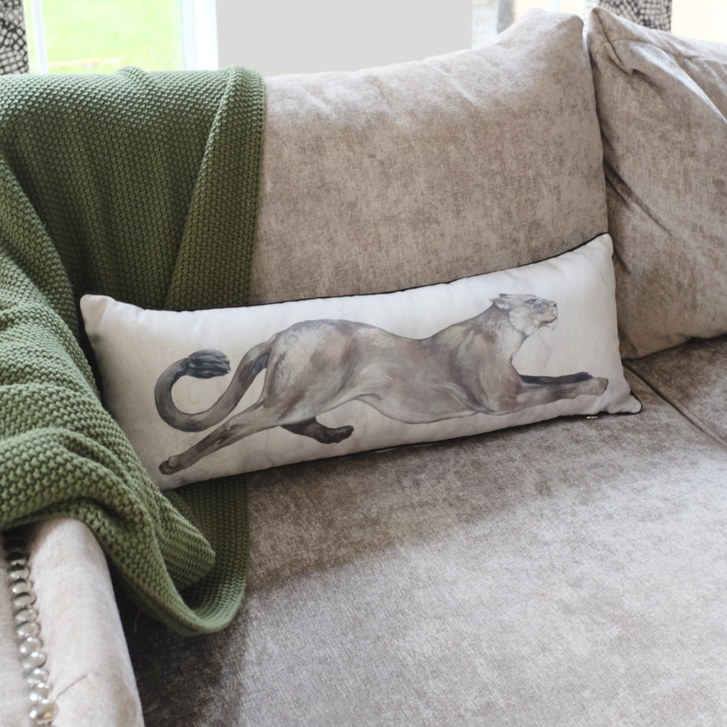Decorative pillow with a lion design on a beige sofa with a green blanket.