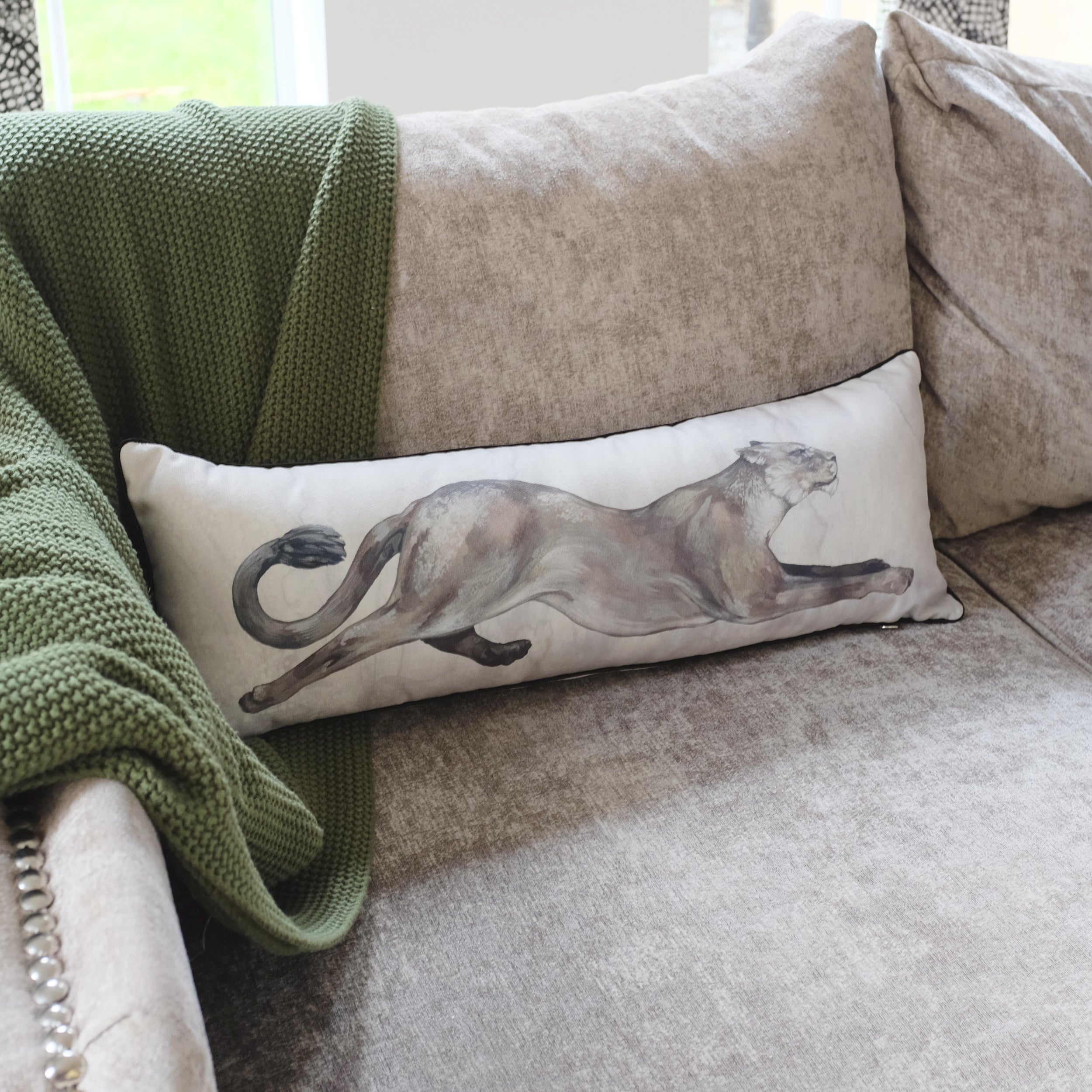 Decorative pillow with a lion design on a beige sofa with a green blanket.