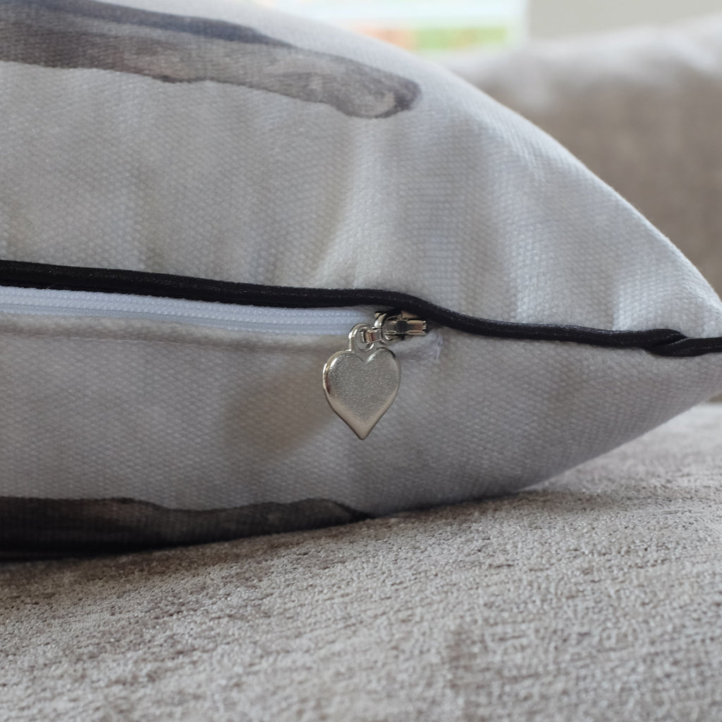 Gray pillow with a zipper and heart-shaped charm on a neutral background