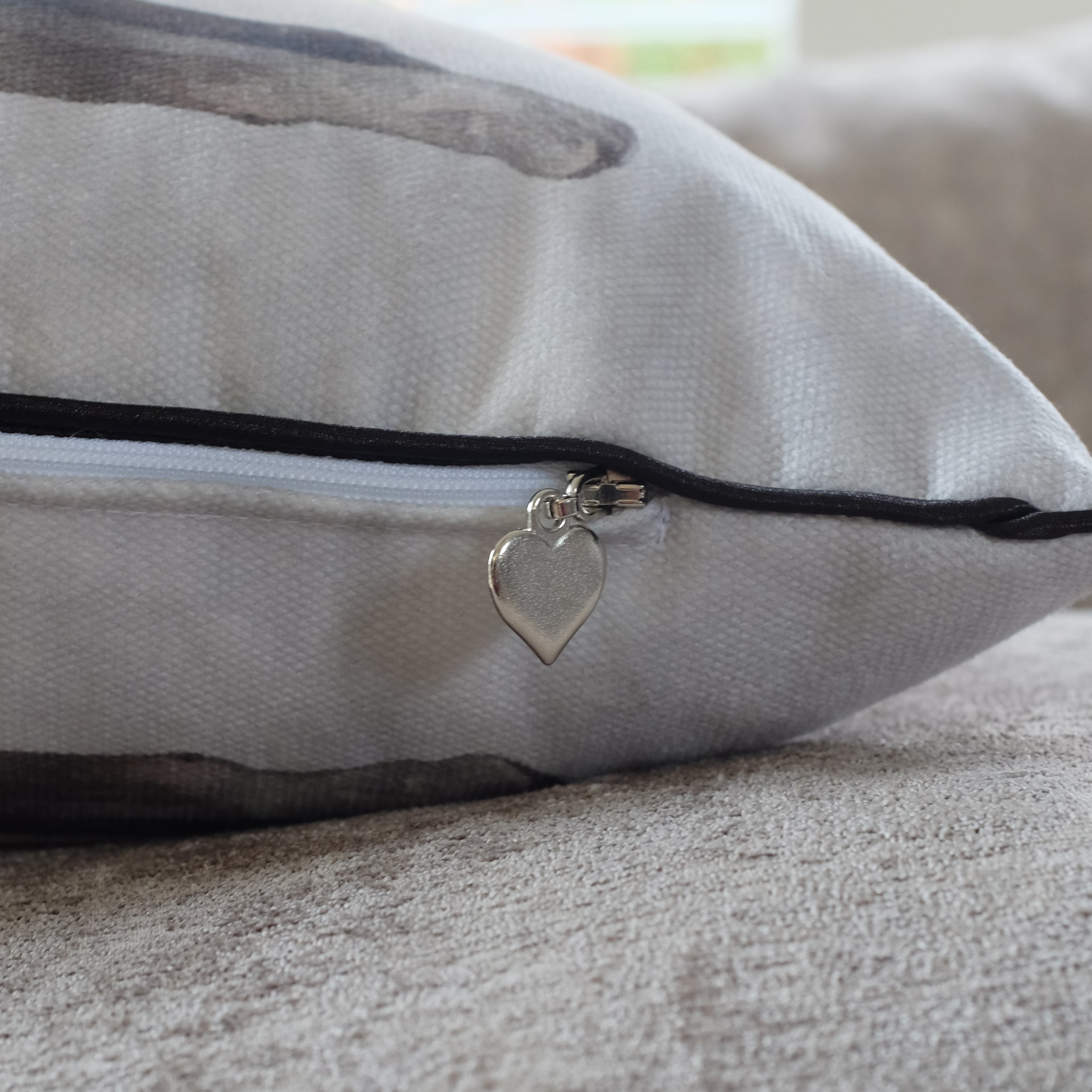Gray pillow with a zipper and heart-shaped charm on a neutral background