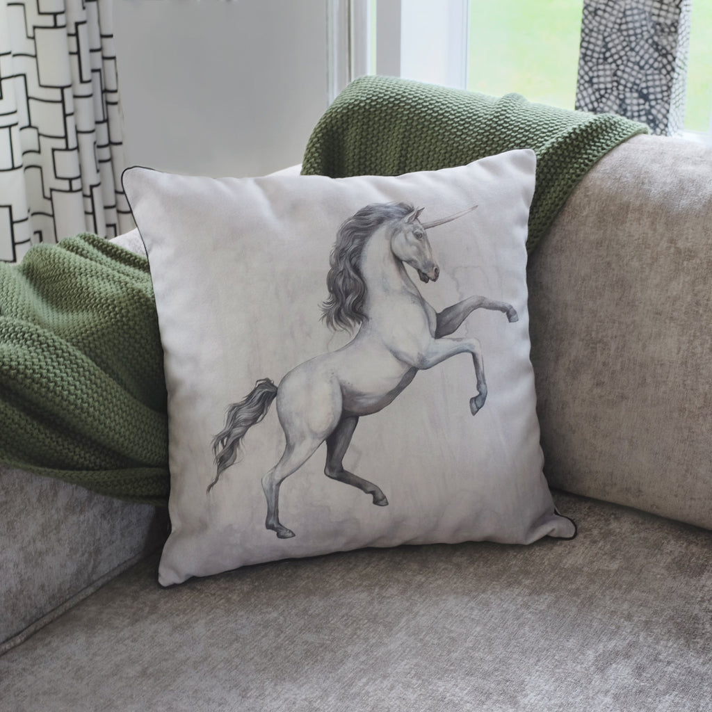 Decorative pillow with a unicorn design on a couch with green blanket