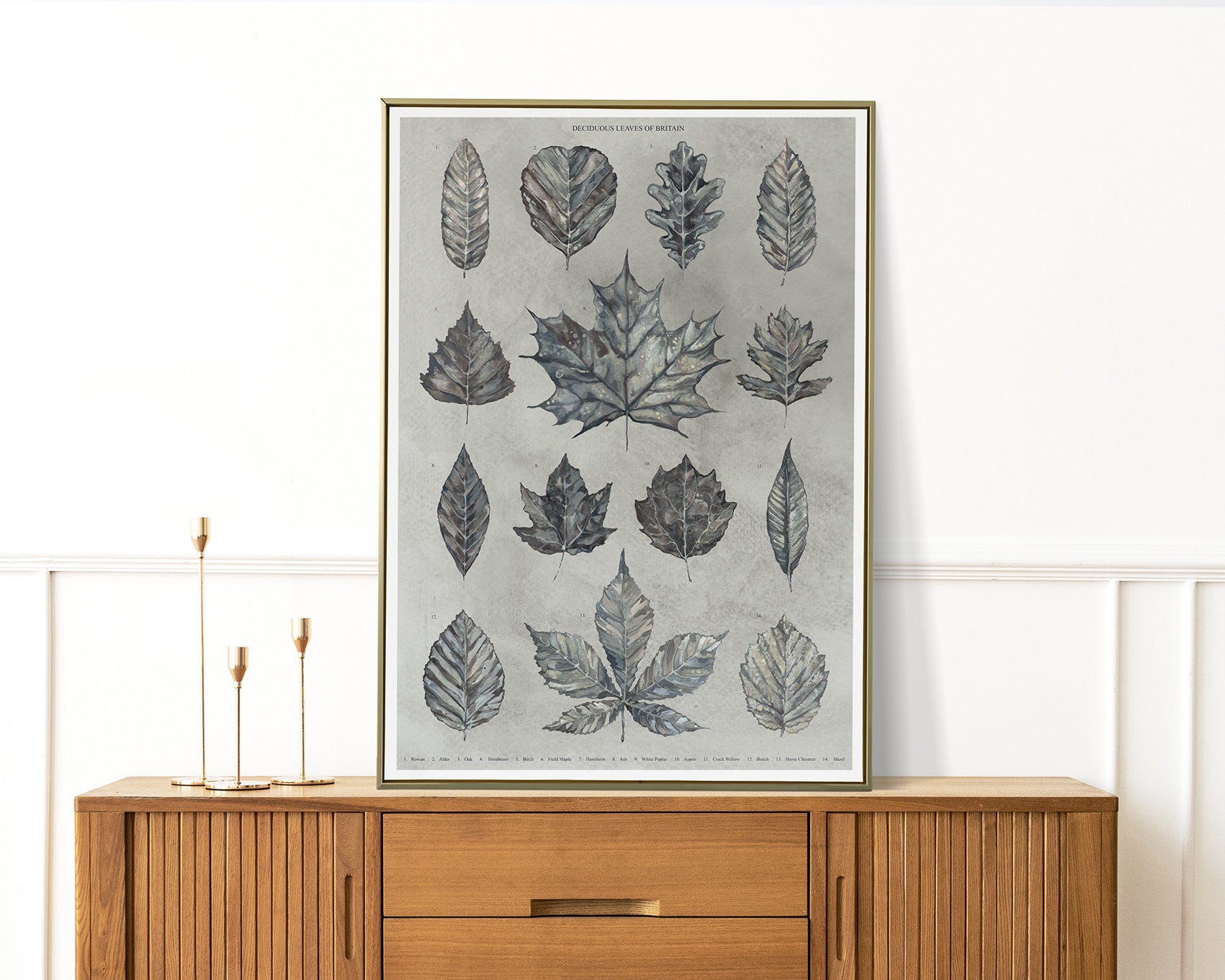 Framed artwork with grey leaf patterns on a wall above a wooden cabinet.